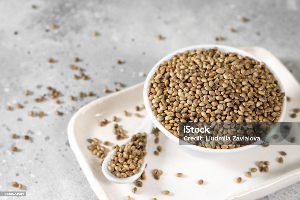 Hemp seeds. Peeled and whole dried hemp seeds in a white ceramic bowl on a light gray kitchen table. Hemp Seeds for Cooking Hemp Seed Stock Photo
