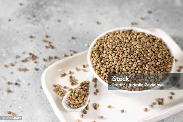 Hemp Seeds Peeled And Whole Dried Hemp Seeds In A White Ceramic Bowl On A Light Gray Kitchen Table Hemp Seeds For Cooking Stock Photo - Download Image Now