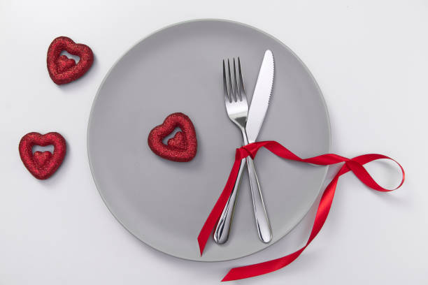 istock Valentine's day festive table setting, flat lay with red heart shape on gray plate, fork, knife and red ribbons on white table. Love dating concept. Place your text and copy space 1300524662