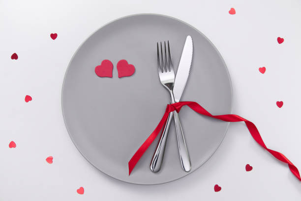 istock Valentine's day festive table setting, flat lay with red heart shape on gray plate, fork, knife and red ribbons on white table. Love dating concept. Place your text and copy space 1300524830