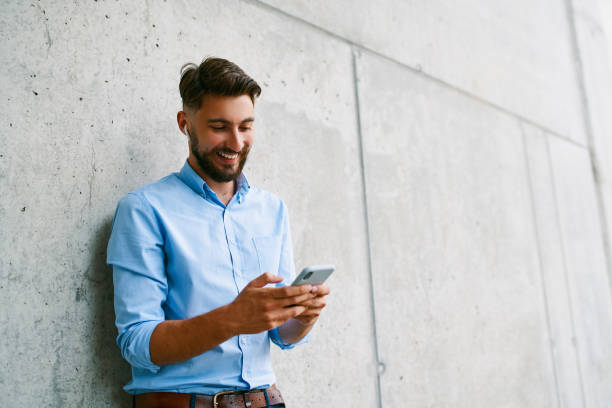 istock Young man texting with mobile phone standing in the city against concrete wall 1300525541