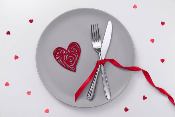 istock Valentine's day festive table setting, flat lay with red heart shape on gray plate, fork, knife and red ribbons on white table. Love dating concept. Place your text and copy space 1300525697
