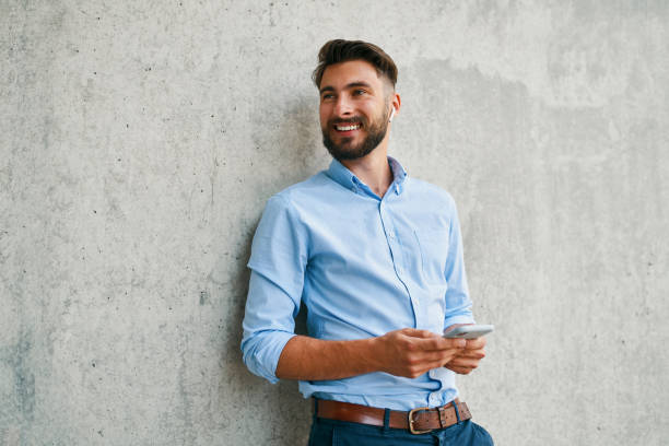 istock Young man talking on phone through wireless headphones and looking away while leaning on wall in the city 1300525761
