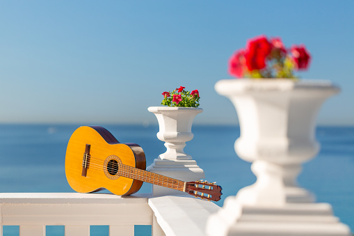Spanish guitar lying on a white balustrade in front of the blue sky and sea for holiday concepts.