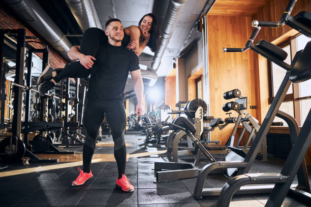 istock Happy young man holding girlfriend on shoulders in gym 1300528038