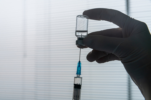 Nurse preparing to give a COVID-19 vaccine close-up on the ampoule and the syringe - pandemic protocols