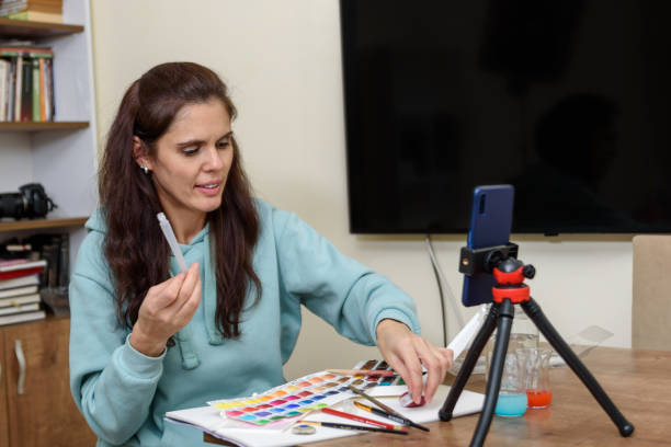istock Online art lesson during quarantine. Smartphone with tripod close up, teacher talks about brushes and how to draw 1300529921