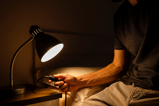 Young man turning on lamp on nightstand beside bed.