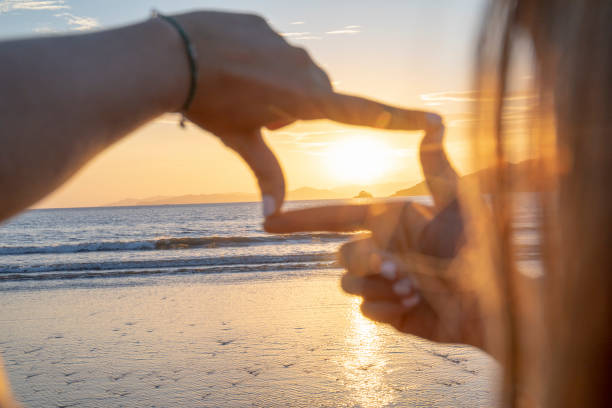 istock Young woman frames sunrise over Pacific Ocean with hands 1300533331