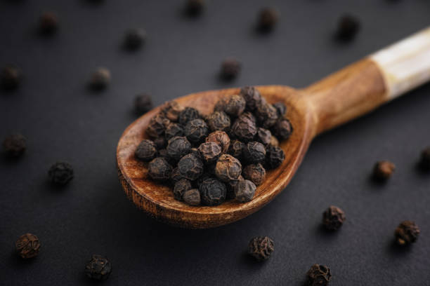 Organic whole black peppercorns in a wooden spoon Organic whole black peppercorns in a wooden spoon. Low key. Close up. black peppercorn photos stock pictures, royalty-free photos & images