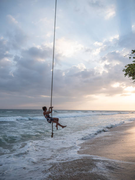 istock Woman plays on rope swing above sea 1300538306