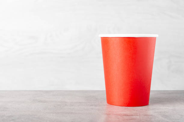 A red paper cup stands on a wooden table.