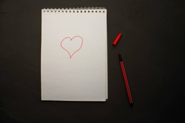 istock A red marker with a white notebook on a black background. View from above. Colorful pens with a large notebook. The heart is drawn on the notebook 1300539747
