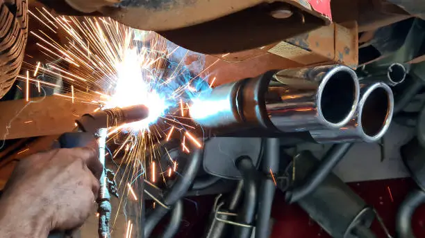 Mechanic or welder is fixing a car exhaust system by welding the exhaust pipe