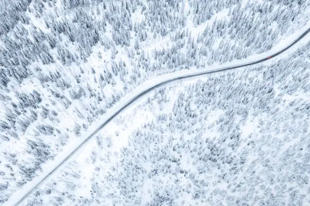 Aerial drone view of road in winter forest with red car.