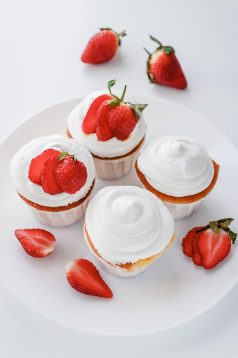 Homemade muffins with meringue caps and strawberries on white background top view