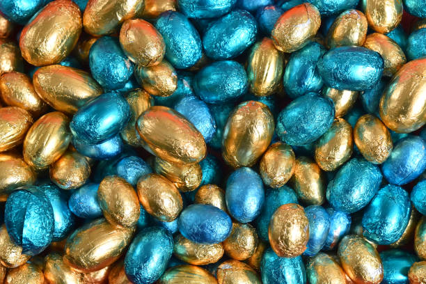 Blue, gold and turquoise foil wrapped chocolate easter eggs, against a black background.
