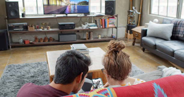 istock Couple Sitting on Couch Looking at Phone on TV 1300547230