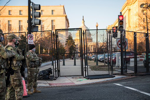 Washington DC, USA - January 21, 2021: Armed members of the National Guard provide security on the perimeter of a recently constructed fence topped with razor wire surrounding the U.S. Capitol Building in Washington DC.