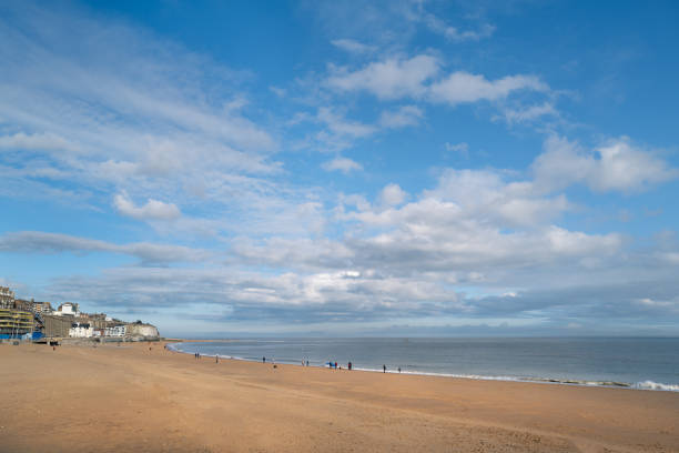 A winter beach on a blue sky day with fluffy white clouds. A few unrecognisable people are walking on the beach. A winter beach on a blue sky day with fluffy white clouds. A few unrecognisable people are walking on the beach. The beach is Ramsgate Main Sands ramsgate stock pictures, royalty-free photos & images