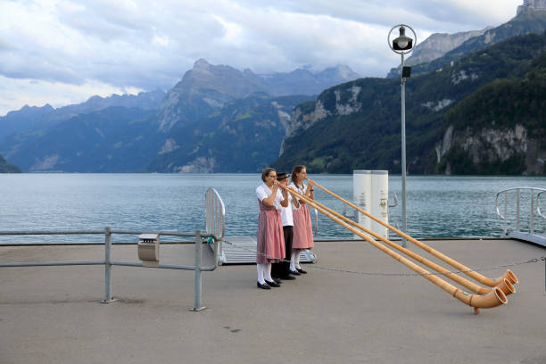 Swiss musicians play alpine horns Brunnen, Switzerland - August 26, 2020: Swiss musicians play alpine horns, which takes place on the pier on the shores of Lake Lecerne. In the distance you can see Alpine Mountains range. It is one of the countless wonderful places that is a tourist attraction often visited by many tourists from all over the world. alpenhorn stock pictures, royalty-free photos & images