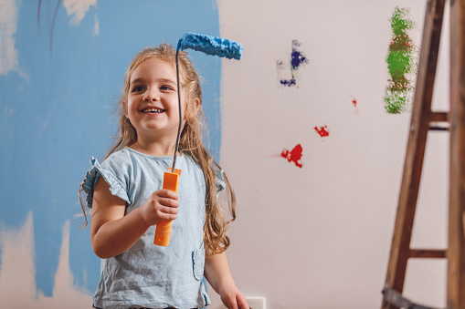 Copy space shot of smiling little girl holding a paint roller and is excited to be painting the wall in her new room.