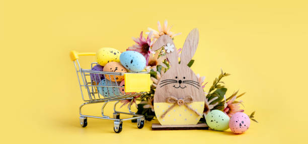 пасхальная композиция с разноцветными яйцами в корзине, деревянным кроликом и весенними цветами на желтом фоне. баннер. - pasch стоковые фото и изображения