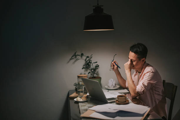 night overwork asian chinese male working late at home dining room emotional stress with his financial bill alone at night - despair finance report business imagens e fotografias de stock