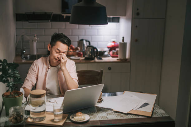 noche exceso de trabajo asiático asiático hombre trabajando hasta tarde en el comedor en casa estrés emocional con su factura financiera solo por la noche - debt fotografías e imágenes de stock