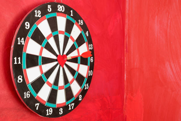Dart arrow on red heart shape in on the bull's eye of dartboard. Pixel shift effect is applied for more details. No people are seen in frame. Shot with a full frame mirrorless camera.