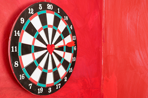 Dart arrow on red heart shape in on the bull's eye of dartboard. Pixel shift effect is applied for more details. No people are seen in frame. Shot with a full frame mirrorless camera.