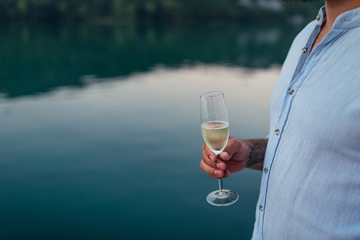 Close up of man's hand holding glass of wine by the river