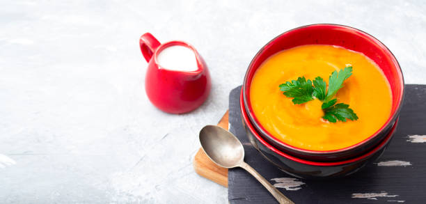 istock Pumpkin and carrot puree soup with cream on a gray stone background. 1300566368