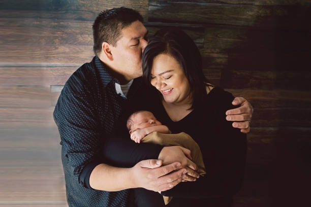 Mother and Father Holding Newborn A man kisses his wife as they hold their newborn baby. indian couple kiss stock pictures, royalty-free photos & images