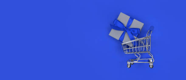istock Supermarket trolley and gift box on blue background with copy space. Shopping concept. 1300569568