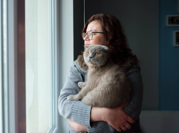 istock Young Woman hugging a cat and looking through the window 1300572497