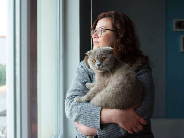istock Young Woman hugging a cat and looking through the window 1300572569