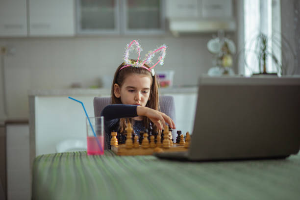 Cute Little Girl Playing Chess with chess master. Online at home education. Photo of one cute little girl playing chess online on a video call with chess master. homeschooling concept. computer chess stock pictures, royalty-free photos & images