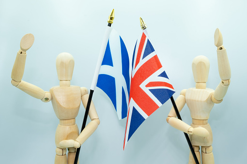 2021: Two wooden mannequins in standing positions, with an arm raised in support of the flag they each hold. One represents Scotland with the Scottish flag, the other represents the United Kingdom with the Union Jack flag. The debate goes on about a second Scottish independence referendum, which is being driven by the Scottish National Party, known as the SNP.