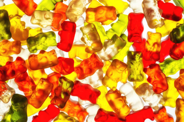Horizontal composition photography of gradient multi colored (red, green, yellow, orange, white etc...) colorful gummy bears candy in a row arrangement close-up studio shot on white background. Picture taken in close-up with selective focus.