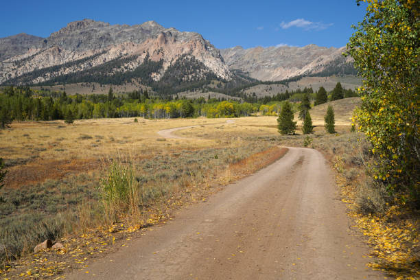 A dirt road leads to mountains on a sunny autumn afternoon. stock photo