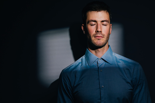 Portrait of a dreamer: a handsome Caucasian man in a blue shirt with eyes closed, a studio shot.