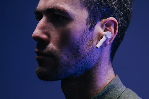 Dark shot of a man listening to music/ a podcast through wireless earphones.