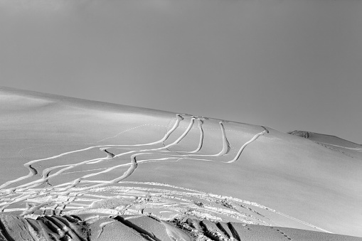 Snowy off-piste ski slope with trace from skis and snowboards at winter night. Black and white toned landscape.