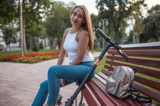 istock Woman sitting on park bench with electric scooter 1300584837