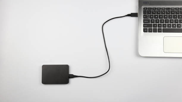 External hard drive connected to laptop External hard drive connected to laptop on white surface. Concept for office, business, education and presentation external hard disk drive stock pictures, royalty-free photos & images