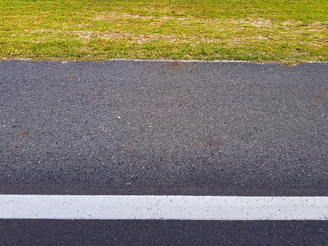 Parallel lines of road marking, asphalt and grassy verge.