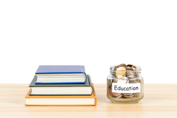 istock Coins in glass jar with label on wooden desk with book stack on white background, concept saving for education and scholarship 1300618545