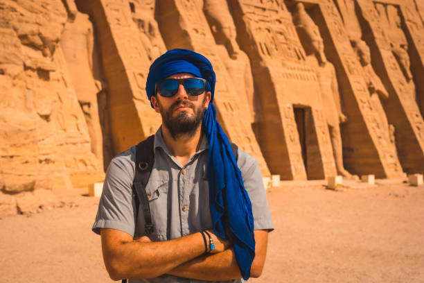 młody mężczyzna ubrany w niebieski turban odwiedzając egipskiej świątyni nefertari w pobliżu abu simbel w południowym egipcie w nubii nad jeziorem nasser. świątynia faraona ramzesa ii, podróżny styl życia - lake nasser zdjęcia i obrazy z banku zdjęć