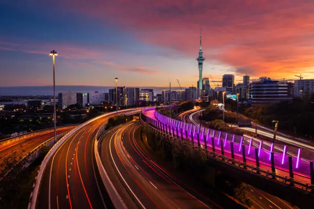 View of Auckland city skyline, Skytower, and motorway with car trails at sunrise.